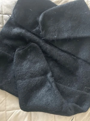 Svart stickad kofta från Lindex - Säljer en mjuk och fluffig mörkgrå halsduk från Lindex. Halsduken har en enkel design och är tillverkad i ett lurvigt material som känns riktigt mysigt. Perfekt att svepa runt halsen för extra värme under kalla dagar.