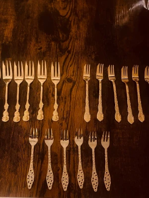 Antika dessertgafflar i guldfärg - Säljer ett set med tolv antika dessertgafflar i guldfärg. Gafflarna har vackra, detaljerade handtag med blommönster och olika dekorativa inslag. Perfekta till fika eller som samlarobjekt för dig som gillar vintage bestick.