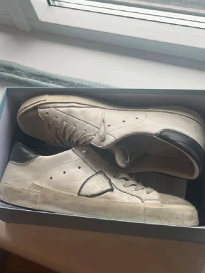 Vita Philippe Model sneakers - Snygga vita sneakers från Philippe Model med svarta detaljer på häl och sidan. Klassisk låg modell med vita skosnören och diskret logga. Tillverkade i läder med gummisula. Perfekta för en clean och stilren look.