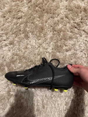 Nike Mercurial svarta fotbollsskor - Säljer ett par svarta Nike Mercurial fotbollsskor med subtila ränder och en diskret Nike-logga på sidan. Skorna har svarta skosnören och gula dobbar för bra grepp på planen. Tillverkade i syntetmaterial för lätt känsla och snabbhet. ÄNDAST ANVÄNDA 3-4 GÅNGER!