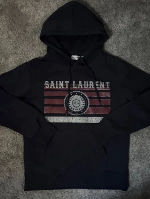 Saint Laurent hoddie - Säljer nu denna snygga saint Lauren hoddie, tröjanw är i jättefint skick då den aldrig är använd✅storlek m (Hör gärna av er vid frågor🙌🏼) , vet ej om den är äkta