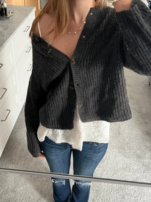Mörkgrå ribbad kofta med knappar - Mysig mörkgrå ribbstickad kofta med flera knappar framtill. Koftan har en avslappnad passform, långa ärmar och rund halsringning. Perfekt att slänga över en topp för en chill look.💗