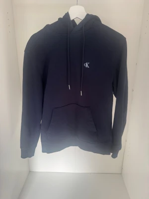 Mörkblå hoodie från Calvin Klein - Snygg mörkblå hoodie från Calvin Klein i storlek xs. Den är andvänd fåtal gånger och är i toppskick. Den har inga tecken på andvändning. Hör av er med funderingar. /Milo