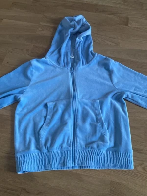 Ljusblå zip hoodie med huva - En ljusblå hoodie med dragkedja framtill och två stora fickor. Hoodien har ribbade muddar vid ärmslut och nederkant samt en rymlig huva. Tillverkad i mjukt tyg som känns skönt mot huden. Perfekt för en avslappnad och chill stil.