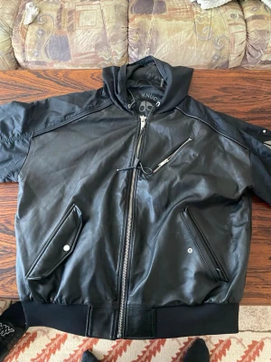 Svart skinnjacka från Moose Knuckles - Snygg svart skinnjacka från Moose Knuckles med dragkedja framtill, två snedställda fickor med tryckknappar och en bröstficka med dragkedja. Jackan har ribbade muddar och en hög krage för extra attityd. Perfekt för dig som vill ha en stilren och cool look.