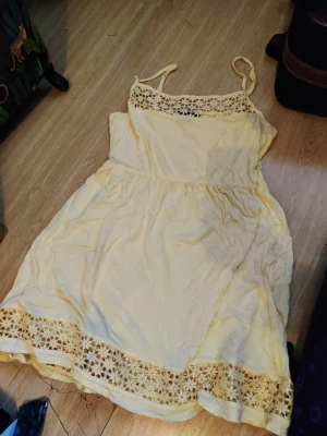 Ljusgul sommarklänning med spets - Söt ljusgul klänning med tunna axelband och fina spetsdetaljer vid halsringning och nederkant. Klänningen har en avslappnad passform och är perfekt för varma dagar. Materialet känns lätt och luftigt.