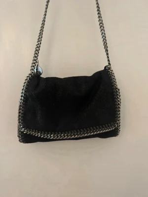 Svart Stella McCartney Falabella väska - Köptes 15 oktober 2022 på vestiare (online kvitto finns som bild) ,vilket betyder att den är äkta. En tråd har gått av som syns på bild, men annars i ett gott skick! 💕 Liten axelbandsväska med långt band (ca 132cm). Väskan är 15×21cm!