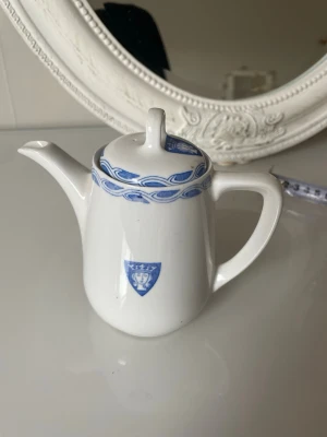 Vit tekanna Gustavsberg - Gustavsberg kaffekanna i porslin med vit glasyr och blå dekor. Klassisk form med lock, pip och handtag. Passar för servering av kaffe eller te. Stämplad Gustavsberg i botten.