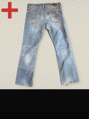 Levi's 527 - Säljer ett par klassiska blå vintage Levi's 527 jeans med bootcut passform och slitna detaljer. Jeansen har fem fickor, ljusa tvättade partier och en röd Levi's-tag på bakfickan. Perfekta för en avslappnad och trendig look. Storlek 34/32 