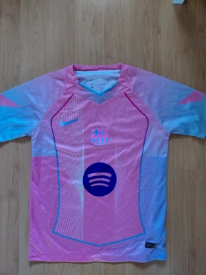 Rosa FC Barcelona matchtröja Nike - Säljer en rosa FC Barcelona matchtröja från Nike med Spotify-logga på bröstet. Tröjan har ljusblå och vita detaljer, klubbemblem och Nike-logga på framsidan. Materialet är lätt och andas, perfekt för fotboll eller träning.