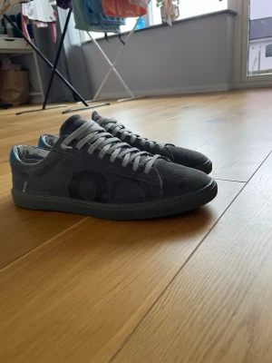 Gråa sneakers från Oliver Cabell - Snygga gråa sneakers från Oliver cabell i mocka med  blå detalj på hälen. Klassisk låg modell. Perfekta för en clean och stilren look. Passar till allt. du har varit välvårdad sen jag köpte dem. Fråga om ni har frågor. 