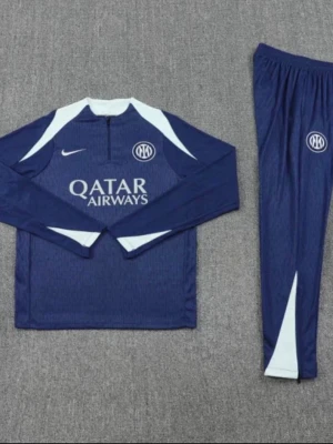 Blå Nike träningsset Inter Miami - Snyggt blått träningsset från Nike och Inter Miami med vita detaljer. Setet består av en långärmad tröja med halv dragkedja och matchande byxor. Båda plaggen har klubbens logga och Qatar Airways tryck på bröstet. Perfekt för träning eller chill.