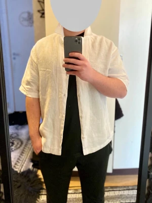 Vit linneskjorta H&M - Säljer en stilren vit skjorta från H&M i luftigt linne. Skjortan har korta ärmar, klassisk krage och knappar framtill. Perfekt för varma dagar och enkel att matcha med olika outfits.