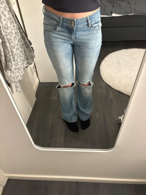 Ljusblå jeans - Ljusblå jeans från Nelly. De har slitningar på knäna och bakficka med knapp. 