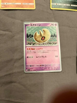 Japansk Pokémonkort Lunatone - Säljer ett japanskt Pokémonkort med Lunatone. Kortet har en lila bakgrund och motiv av Lunatone i ett nattlandskap. Texten är på japanska och kortet har klassisk Pokémon-design med HP och attackvärden.
