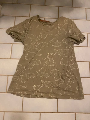 Beige t-shirt med kartmönster Kappahl - Säljer en beige t-shirt från Kappahl med unikt kartmönster i vitt. T-shirten har rund halsringning och korta ärmar. Perfekt för dig som gillar coola prints och vill sticka ut lite extra.