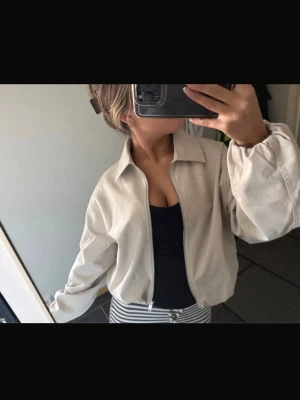 Beige cardiganjacka med dragkedja - Snygg beige cardiganjacka med dragkedja och bred krage. Jackan har en avslappnad passform och ballongärmar som ger en trendig look. Perfekt att slänga över en topp för en chill stil. Passar till både jeans och kjol. Helt ny med prislappen kvar!