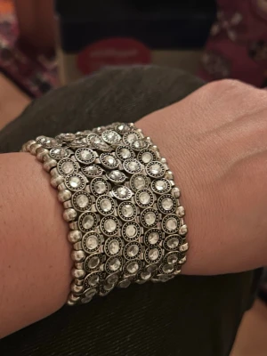 Brett silverfärgat pärlarmband - Snyggt brett armband i silverfärg med flera rader av små, runda pärlor och gnistrande detaljer. Armbandet har en bohemisk och unik design som verkligen sticker ut. Perfekt för dig som gillar accessoarer med lite extra bling och vintagekänsla.