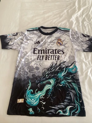 Real Madrid Bellingham Tröja - Håller på att rensa min garderob med fotbollströjor, så säljer denna real tröja med cool design, inga synliga defekter nästan helt oanvänd, max använt den 1-2 gånger när jag kollat på real matcher. Riktigt fin nu till sommaren och med en unik design som är väldigt efterfrågad.