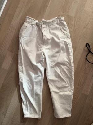 Vita byxor från ZARA i storlek EU 42 - Vita byxor från ZARA i storlek EU 42. Hög midja med paperbag-modell och bekväm passform. Mjukt bomullstyg och snygg, avslappnad stil. Perfekta till vår och sommar. Fint skick.