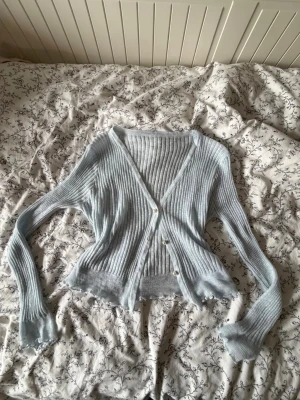 Ljusblå tunn kofta med v-ringning - Säljer en ljusblå ribbad stretchig kofta med v-ringning och 4 knappar framtill, den glänser lite i ljuset . Koftan är något croppad med vågig kant nedtill. Perfekt för sommaren och att ha över klänning. Aldrig använd.  Nypris 176kr, fick i present💗 pris kan ev diskuteras