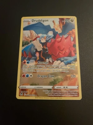 Pokémonkort Druddigon TG05 - Säljer ett Pokémonkort med Druddigon motiv, nummer TG05 från Sword & Shield-serien. Kortet har färgstark illustration med blå, röd och gul ram. Materialet är klassiskt glansigt papp som alla officiella Pokémonkort. Perfekt för samlare eller dig som vill utöka din lek.