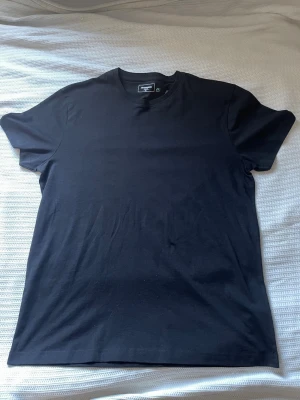 Svart basic t-shirt från Dressman - En enkel svart t-shirt med rund hals och korta ärmar. Tillverkad i mjukt bomullstyg som känns skönt mot huden. Perfekt att matcha med jeans eller shorts för en clean och stilren look. Storleken är XL och är ny med prislapp, du tjänar 100 spänn på köpet 😉