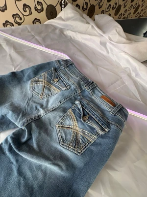 Blå bootcut jeans med broderade fickor - Säljer ett par ljusblå bootcut jeans från wall flower med snygga broderade detaljer på bakfickorna och knappstängning. Jeansen har klassisk femficksmodell och är tillverkade i mjuk denim med lätt tvättad look. Perfekta för en avslappnad men trendig stil.