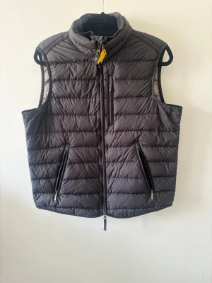 Mörkgrå dunväst från Parajumpers - Snygg mörkgrå dunväst från Parajumpers med gul detalj vid kragen, ståkrage och tre dragkedjeförsedda fickor. Västen har quiltad design och är perfekt för lager-på-lager. Klassisk och sportig look med hög komfort.