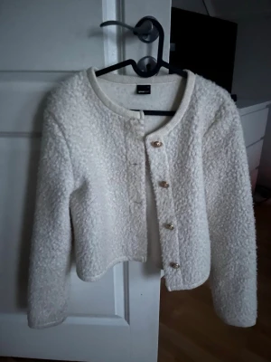 Vit cardigan med guldknappar - Fin vit teddy-cardigan från Gina. Jackan har en croppad passform och är endast använd 2 gånger. Perfekt för lager på lager både för finare tillfällen eller att bara ha på sommaren.