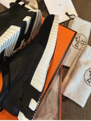 H skorna - Snygga svarta märkes sneakers med chunky vit sula och svarta detaljer på sidan. Skorna har en modern design med blandning av läder och textil, samt svarta skosnören. Perfekta för dig som gillar exklusiva och trendiga sneakers.