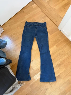 Blå bootcut jeans med slitna benslut - Säljer ett par blå bootcut jeans, slitna vid bensluten. Jeansen har låg midja.
