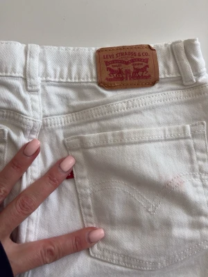 Vita bootcut jeans från Levi's - Säljer ett par vita jeans från Levi's med bootcut passform. Klassisk femficksmodell med Levi's ikoniska läderpatch bak i midjan och röd logotagg vid bakfickan. Tillverkade i kraftig denim, perfekta för en clean och fräsch look.