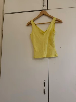 Gul ärmlös linnetopp - Snygg gul linnetopp med v-ringning och breda axelband. Perfekt för varma dagar och enkel att matcha med jeans eller kjol. Toppens material känns mjukt och bekvämt mot huden.