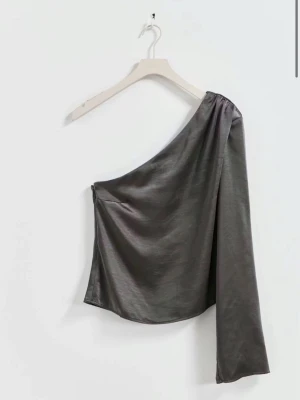 Grå oneshoulder topp i satin - Snygg grå oneshoulder topp i glansigt satinmaterial med lång ärm på ena sidan.