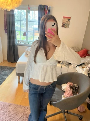 Vit omlottopp med volang och knyt🥰 - Säljer en vit omlottopp med v-ringning, volangkant och långa ärmar. Toppen har knyt i midjan och är croppad vilket ger en trendig look. Perfekt att styla med jeans eller kjol för en fräsch outfit.