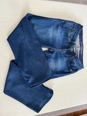 Blå bootcut jeans från Cross Jeans - Säljer ett par snygga blå bootcut jeans från Cross Jeans med klassisk femficksmodell och slitningar framtill. Jeansen har normal midja och är tillverkade i ett mjukt denimtyg med lite stretch för extra komfort. Perfekta till en avslappnad stil.
