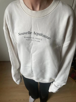 Vit sweatshirt  - Vit sweatshirt med tryck 'Nouvelle Aquitaine Bordeaux, France Port de la Lune' på bröstet. Tröjan har rund halsringning och långa ärmar. Mjuk och bekväm bomullskänsla, perfekt för en chill look.