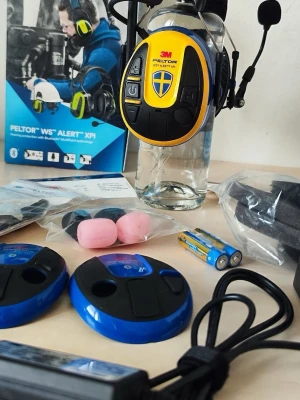 3M Peltor WS Alert XPI hörlurar - Bluetooth-hörlurar från 3M Peltor i blå och svart design med gula detaljer. Over-ear-modell med inbyggd mikrofon, stora vadderade kåpor och robust bygel. Levereras med laddare, batterier, extra öronkuddar och tillbehör. Perfekt för trådlös kommunikation.