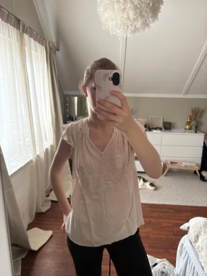 Ljusrosa blus med volangärmar - Söt ljusrosa blus med v-ringning och volangdetaljer vid axlarna. Blusen är i ett tunt, mjukt tyg som faller snyggt och har en avslappnad passform. Perfekt för en trendig och feminin look.