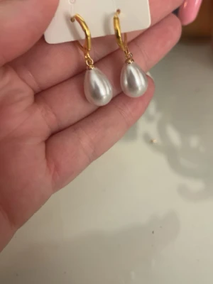Guldiga örhängen med droppformad pärla - Snygga örhängen med guldfärgade hoops och droppformade pärlor i vitt. Perfekta för att ge en elegant touch till din stil. Klassisk design som passar till många olika looks.