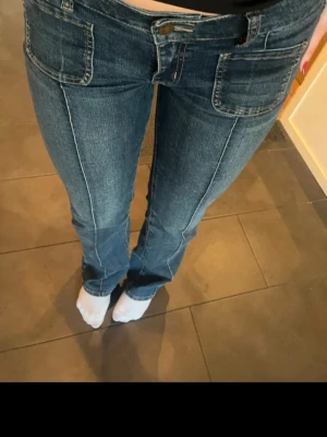 Mörkblå bootcut jeans med fickor - Säljer ett par mörkblå bootcut jeans med markerade sömmar och stora fickor framtill. Jeansen har normal midja och klassisk femficksdesign. Materialet är denim med lätt stretch för skön passform. Perfekta för en avslappnad och trendig look.
