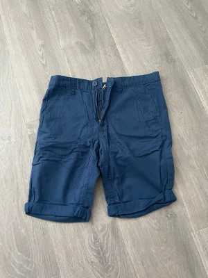 Mörkblå bomullsshorts med dragkedja - Snygga mörkblå shorts i bomull med klassisk passform. Shortsen har uppvikta benslut, sidofickor fram och bakfickor med knapp. Stängs med knapp och dragkedja. Perfekta för sommardagar och enkel att matcha med olika stilar.