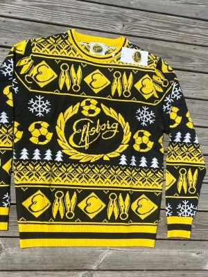Gul och svart Elfsborg tröja - Snygg tröja i svart och gult från Elfsborg med klubbens logga, fotbollar, snöflingor och granar. Tröjan har rund hals och ribbade muddar. Perfekt för dig som vill visa ditt stöd för laget med stil.