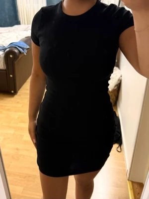 Svart tight kortklänning - En enkel och stilren svart kortklänning med rund halsringning och korta ärmar. Klänningen har en tight passform som framhäver figuren och är perfekt för dig som gillar minimalistisk stil. Materialet känns mjukt och stretchigt.