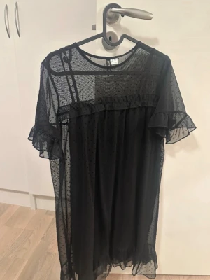 Svart transparent prickig klänning - Säljer en svart transparent klänning med prickigt mönster. Klänningen har volangdetaljer vid ärmslut och nederkant samt korta ärmar. Perfekt för dig som gillar en luftig och trendig look. Storlek S. Aldrig använd! 