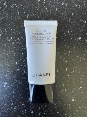 Chanel La Base Illuminatrice Primer - Säljer en Chanel La Base Illuminatrice primer som ger glow och återfuktar huden. Tuben är vit med svart lock och har elegant design. Perfekt för att skapa en jämn och strålande bas innan smink.