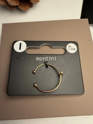 Guldfärgat armband från Montini - Snyggt guldfärgat armband från Montini med minimalistisk design. Armbandet är öppet med två små kulor i ändarna och ett stilrent kors som detalj framtill. Perfekt accessoar för att lyfta din outfit med en trendig touch.