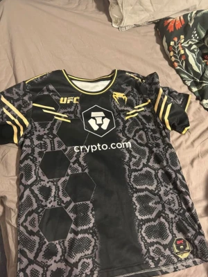 UFC matchtröja svart/guld - Snygg UFC tröja i storlek S (liten i storlek) står Nurmagomedov på ryggen, bra skick (inga hål eller fläckar osv) skriv vid frågor, perfekt för träning eller till vardags 