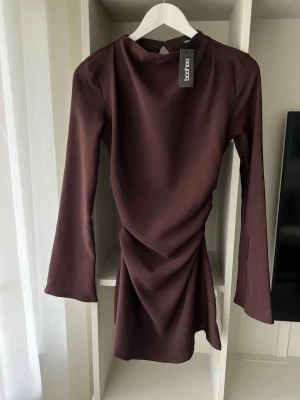 Brun långärmad klänning Boohoo - Säljer en brun långärmad kortklänning från Boohoo med snörning i ryggen, såå fin passform!! Säljer tyvärr pga den kändes för liten, det är storlek 36 men skulle säga att dem känns mer som en 34